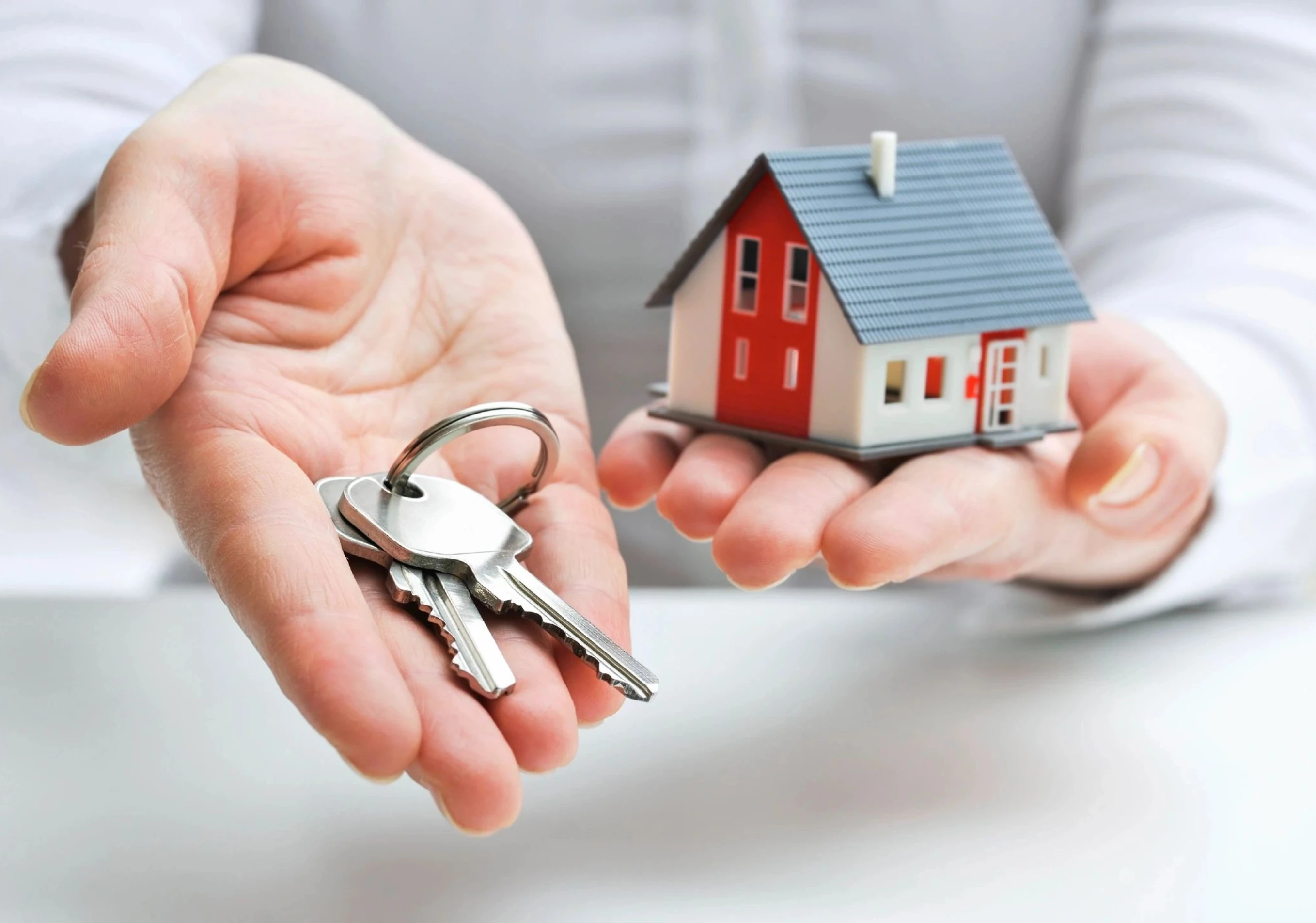 Hands holding a house model and a set of keys.